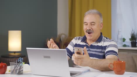 Old-man-working-from-home-enjoys-mobile-apps-on-phone.
